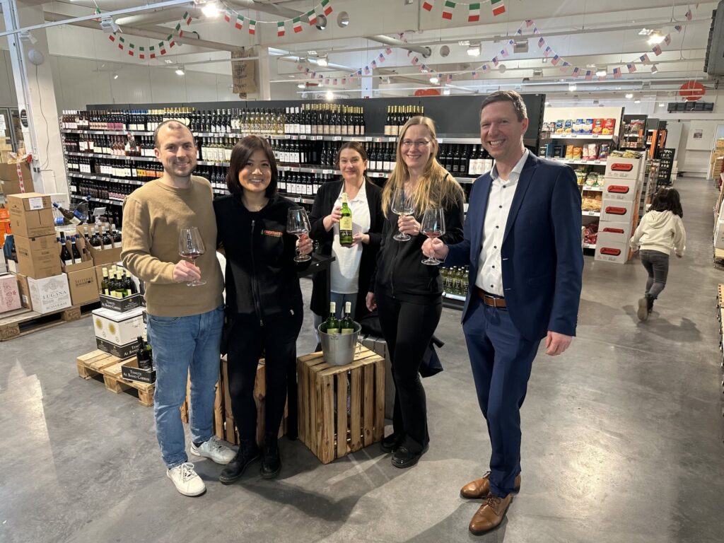 Das Fruchtgarten-Team stößt im Genussmarktplatz vor dem Weinregal mit einem Glas Wein an